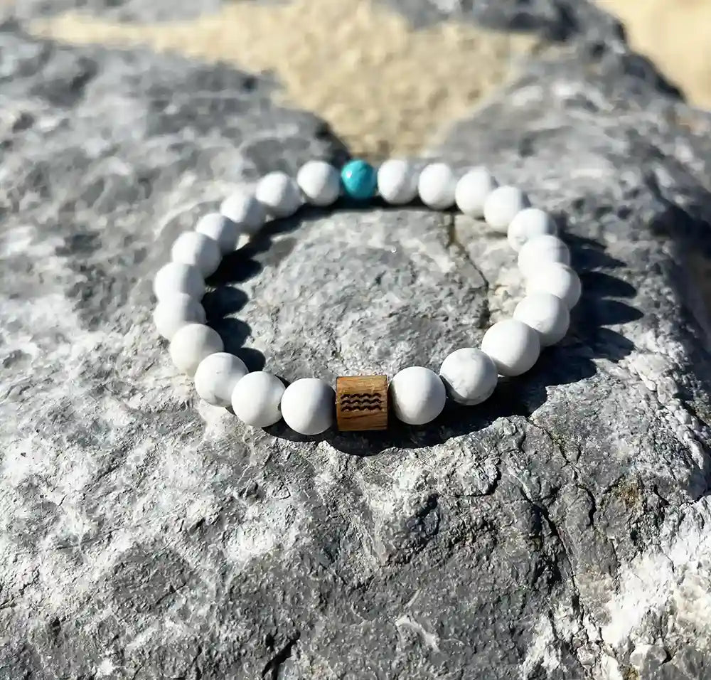 bracelet de perles blanche avec une perle bleu. Posé sur un roché