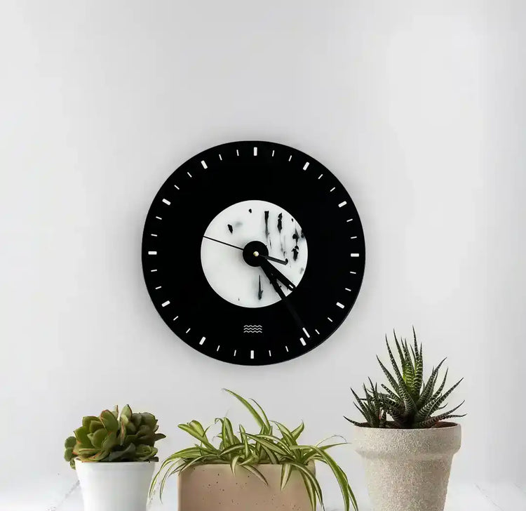 Horloge noir et blanche tachetée accrochée au mur devant 3 petits pots de fleurs